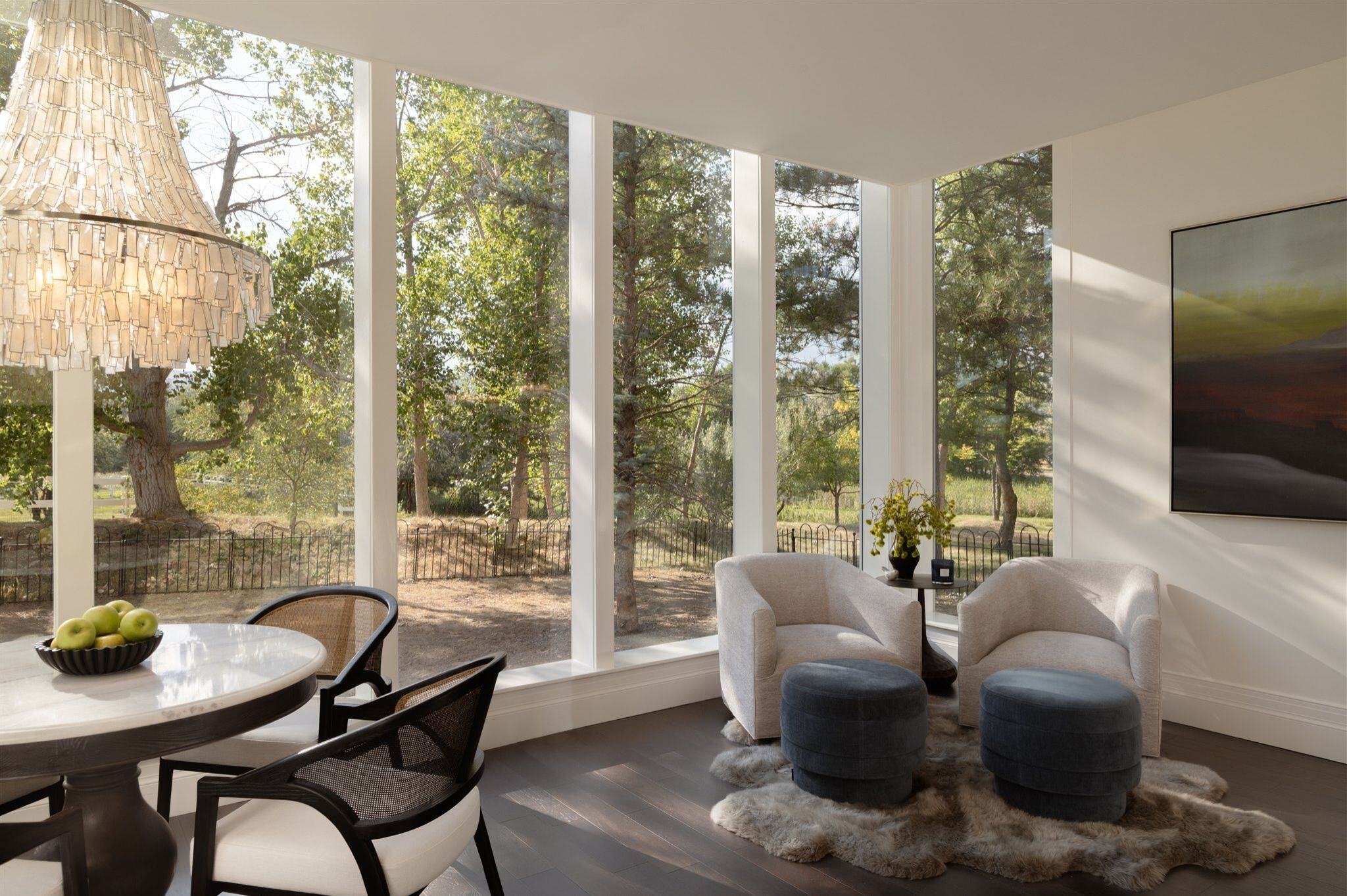 Luxury home sunroom with floor to ceiling windows, dark wood floors, white walls, and seating areas