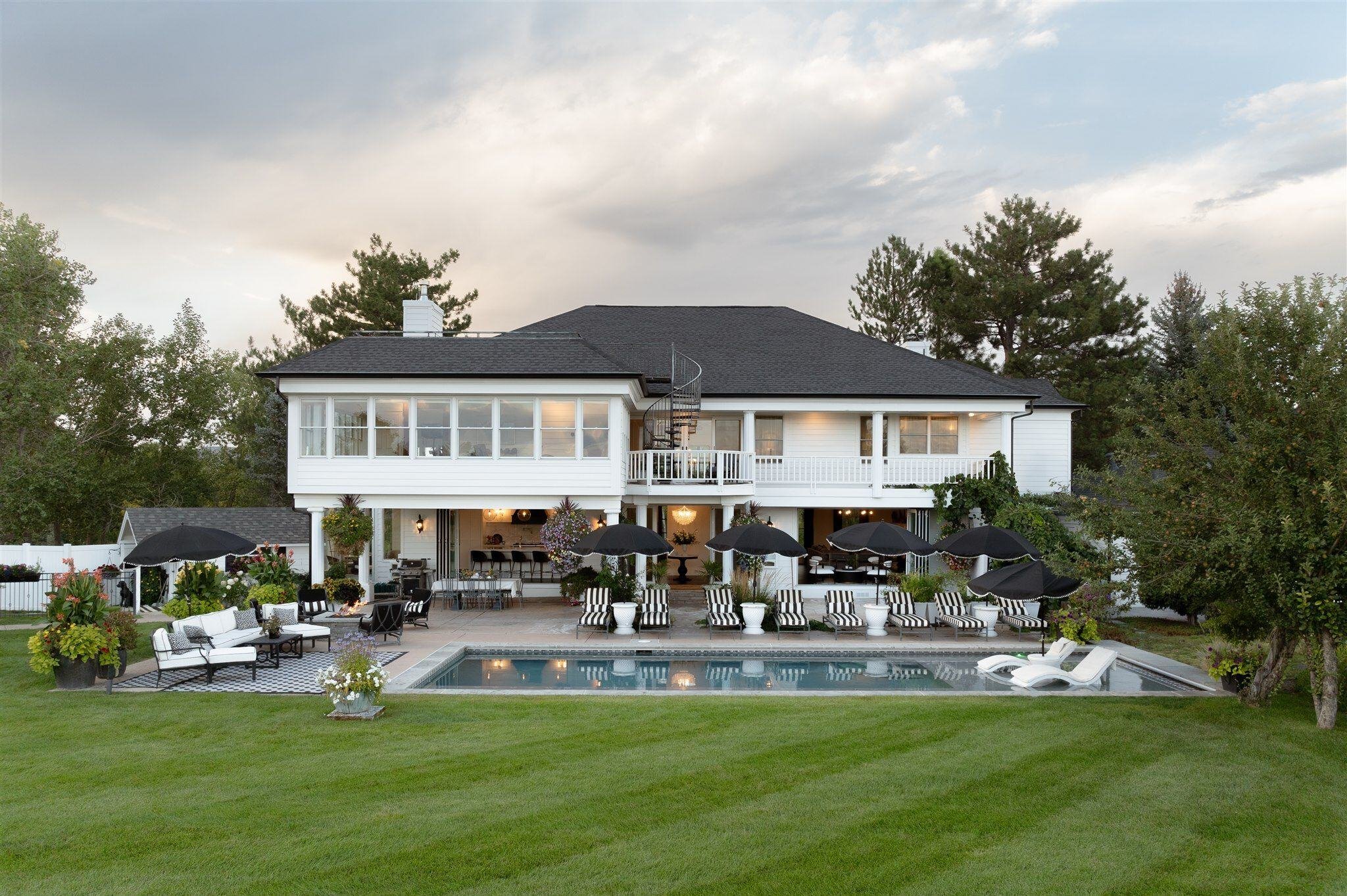 Large luxury home backyard with a pool and black and white lounge chairs and umbrellas