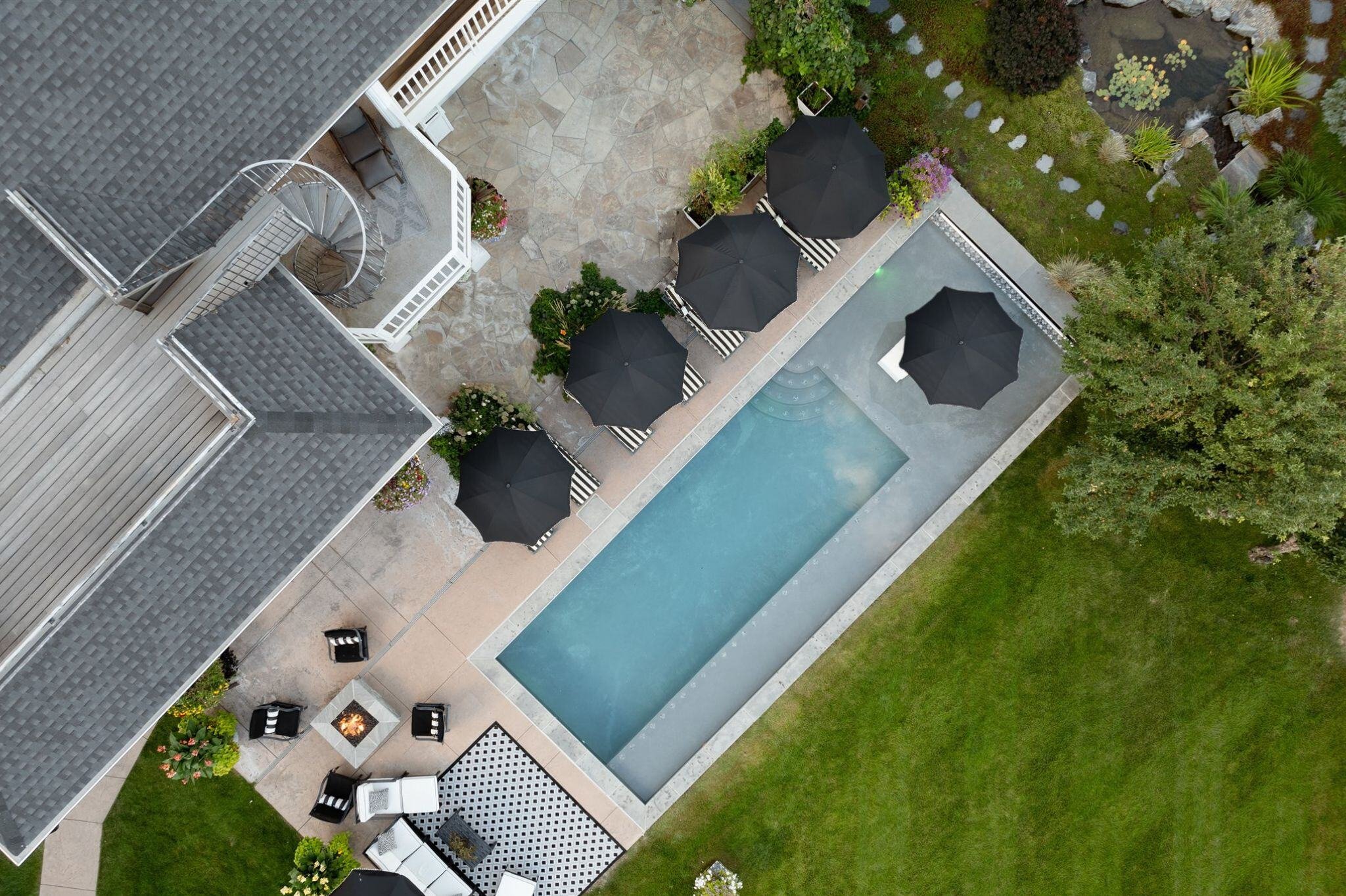 bird's eye view of backyard pool and patio with black and white lounge chairs and umbrellas