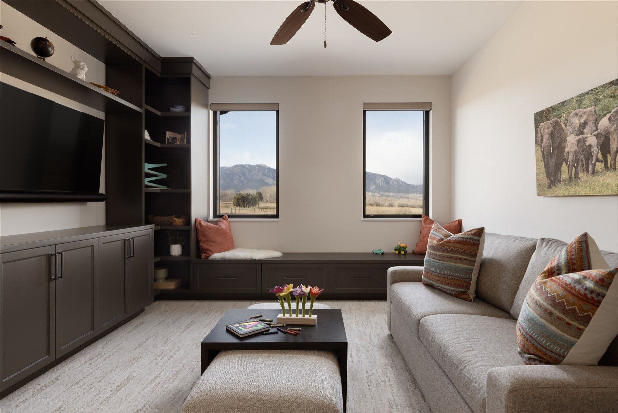 lounge area in a custom built colorado home with a tv and couch, window nook, and views of mountains out of two windows