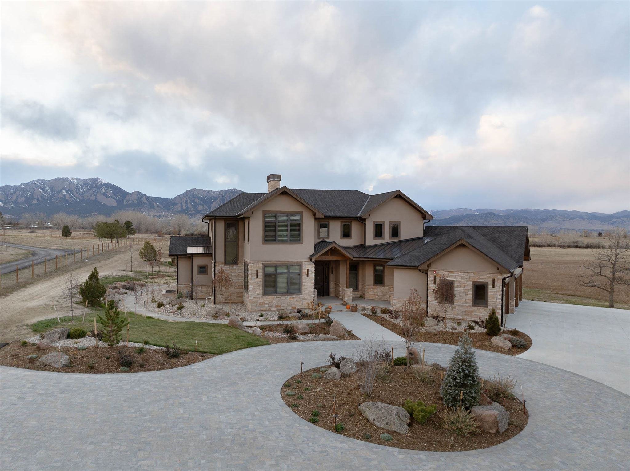 exterior view of a large home remodel with mountain views, warm tan/brown stone exterior, and a large gray stone driveway