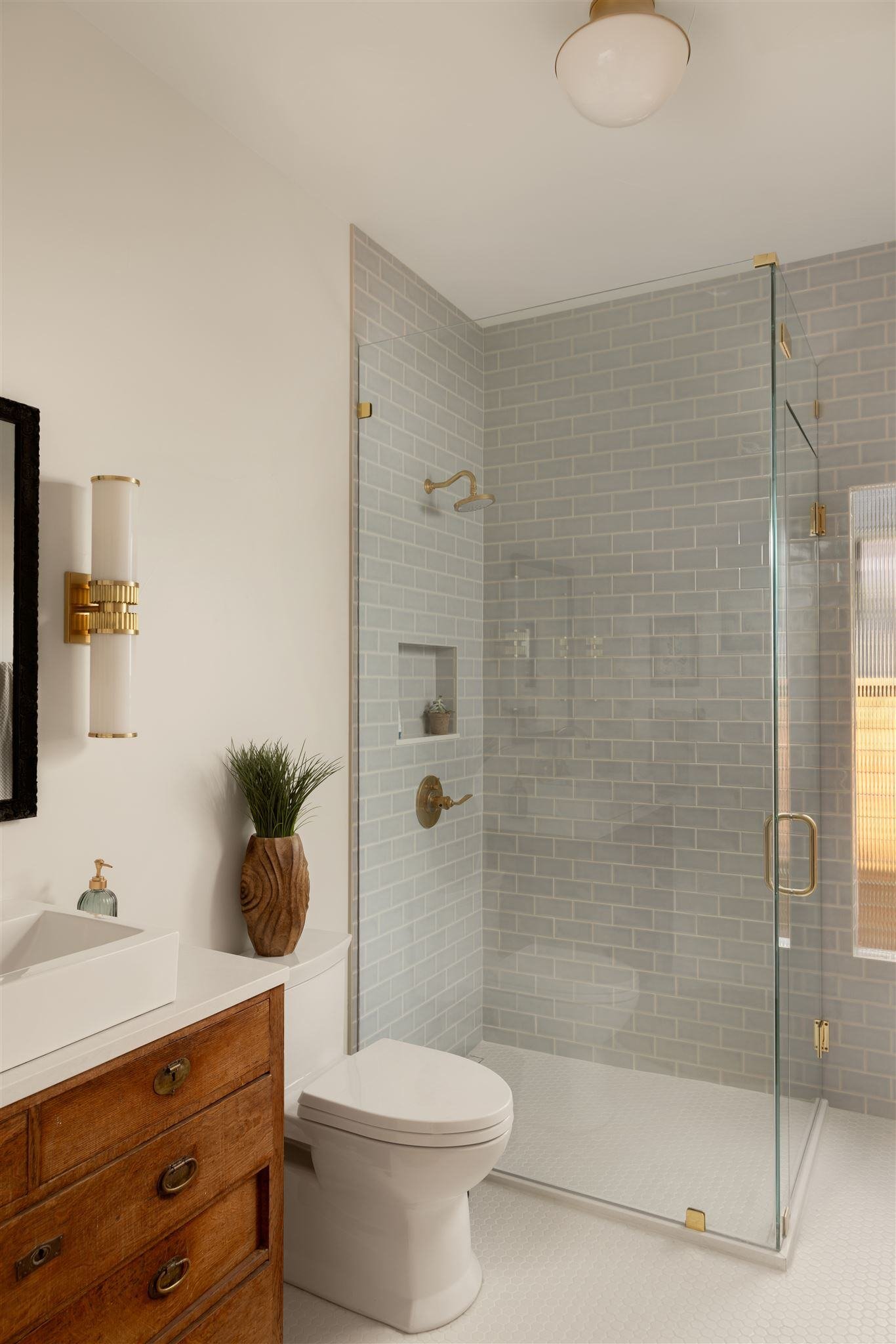 Bathroom remodel with frameless glass shower, wooden bathroom vanity, and light blue and white tiles/walls