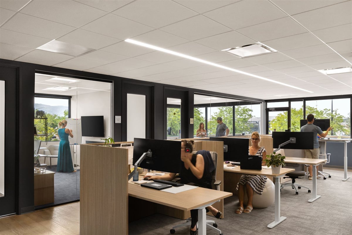 Open layout office space with people sitting at desks, standing at desks, and working on white boards