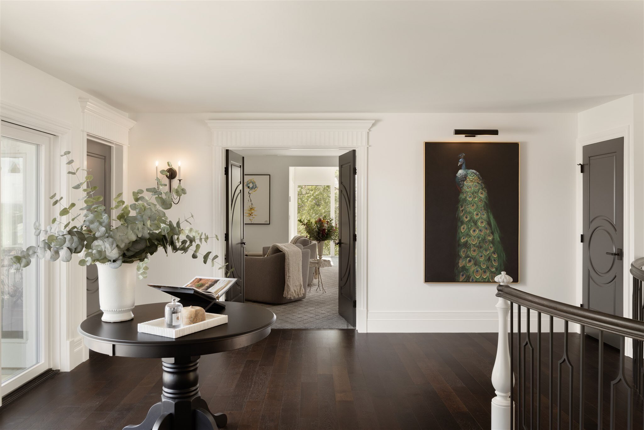 upstairs hallway of luxury home with dark floors, white walls, and a peacock painting