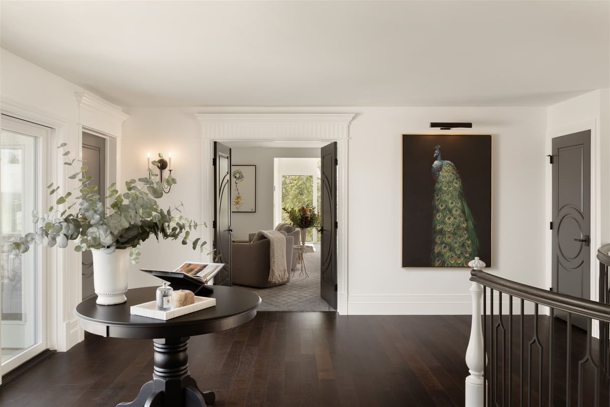 upstairs hallway of luxury home with dark floors, white walls, and a peacock painting