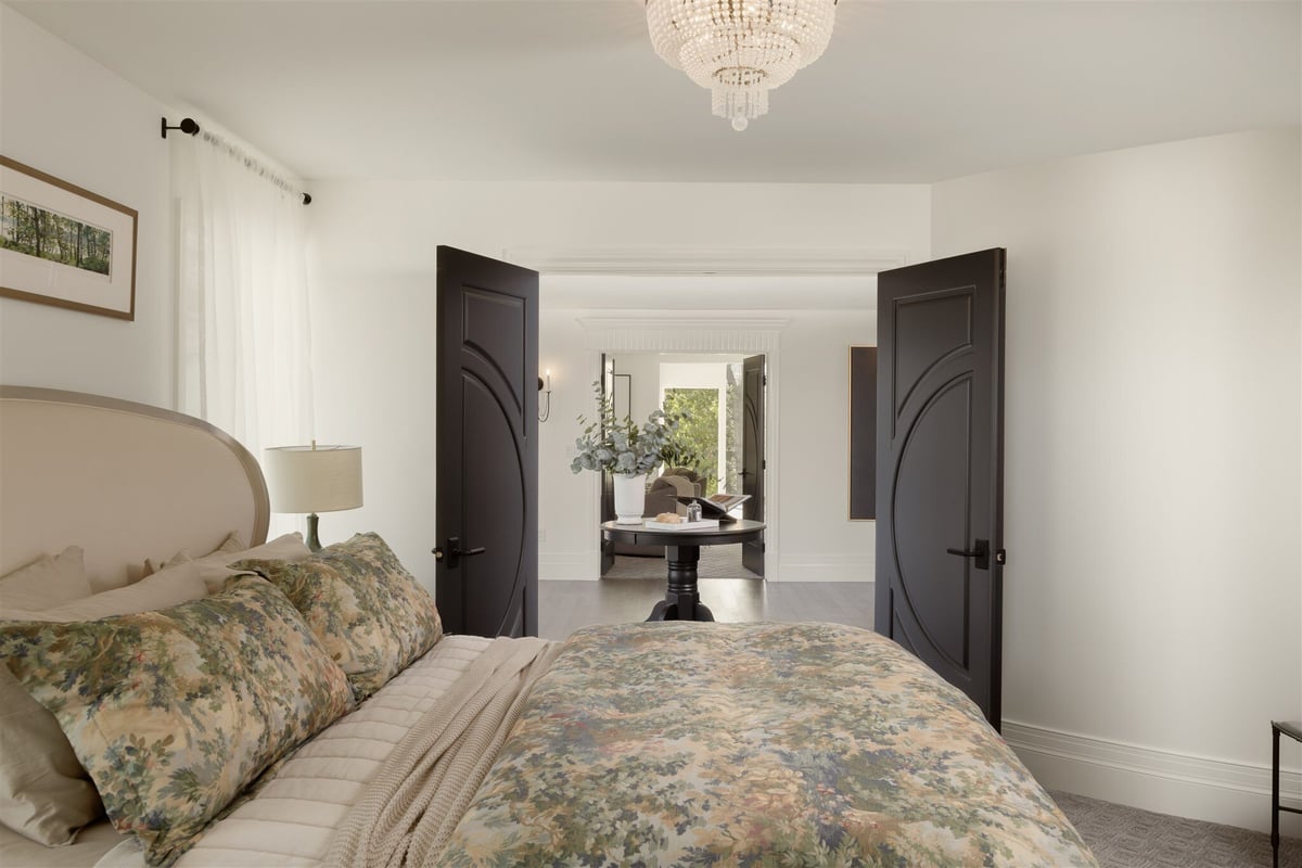 primary bedroom with double black doors and a chandelier