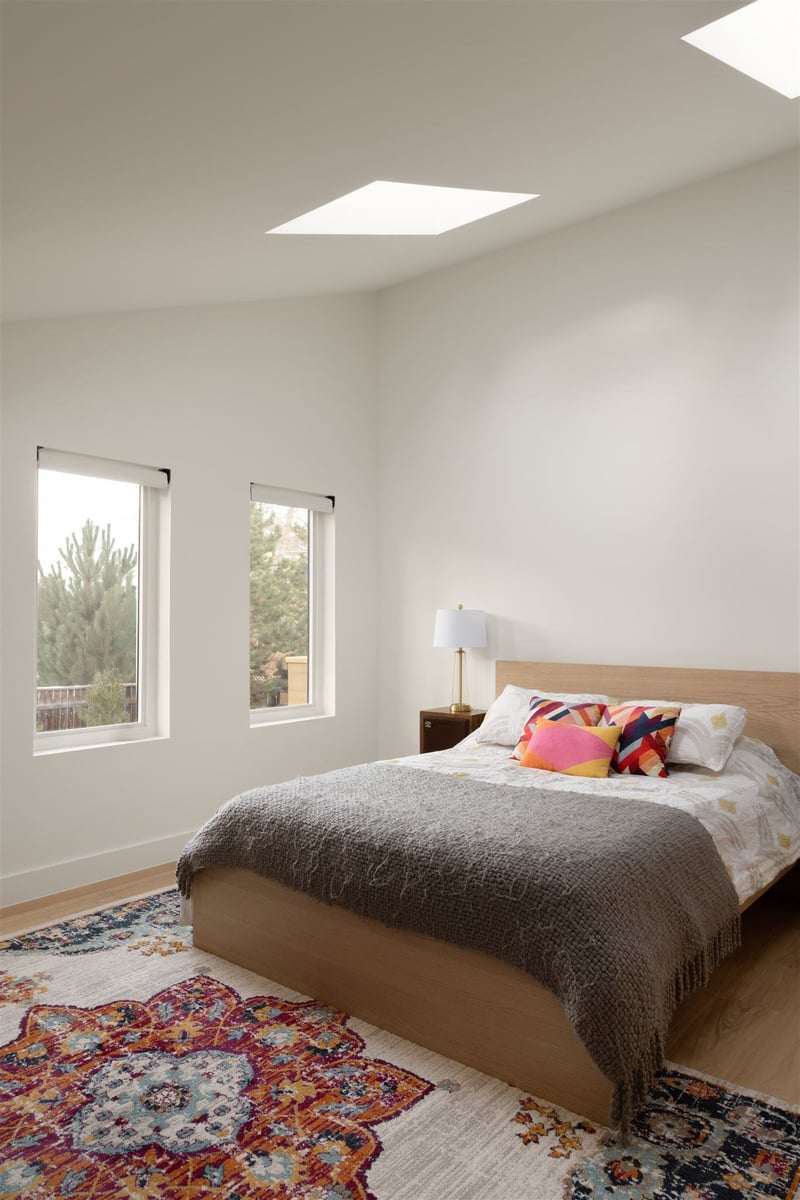 bedroom with white walls, slanted ceiling, and colorful rug and wooden floors