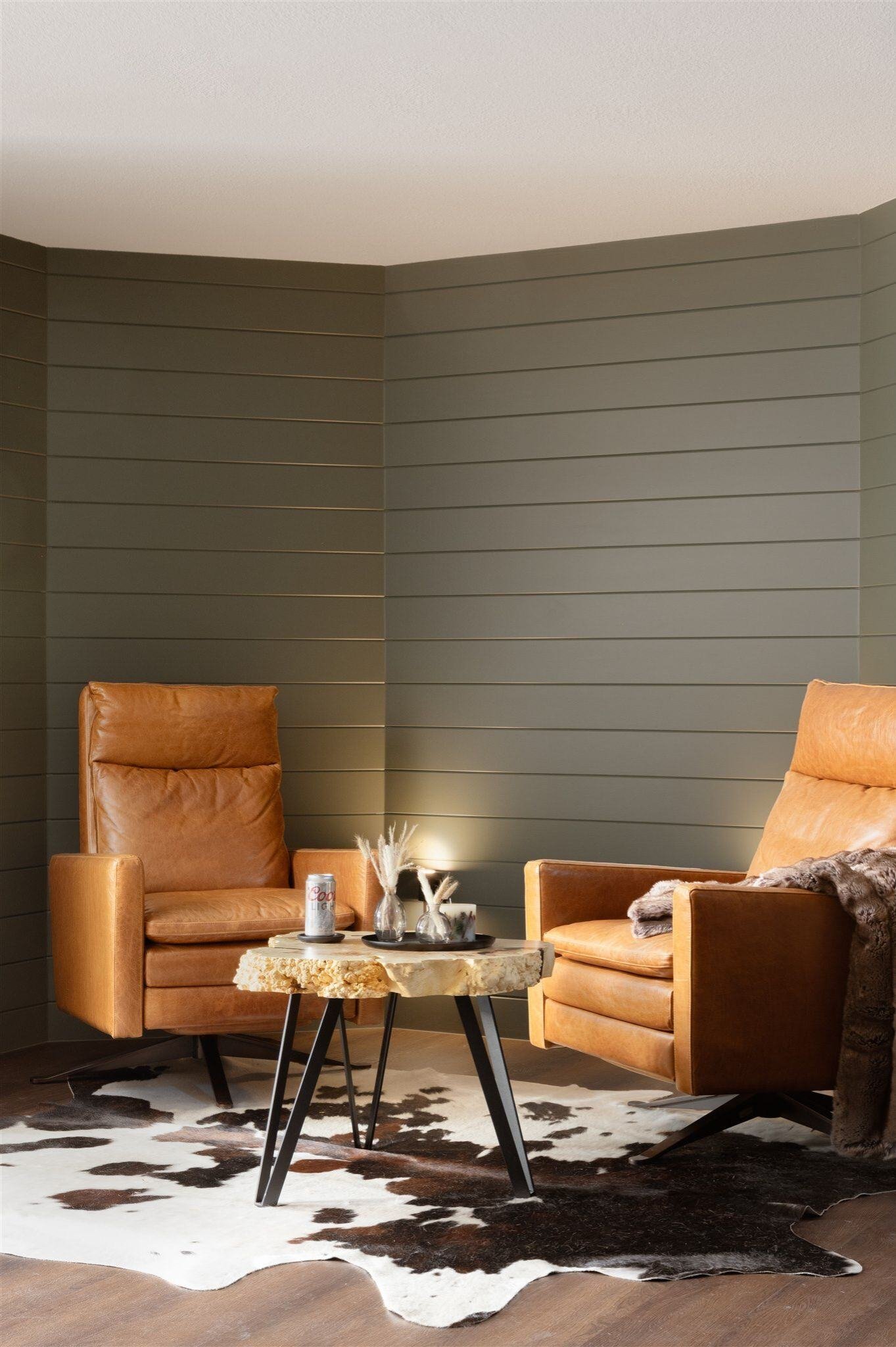 small seating area with two cushioned leather chairs, shiplap walls, and small table with candles.